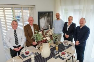 Picture showing five people standing around table in the showhome including the artist Simon King-Underwood standing next to his artwork